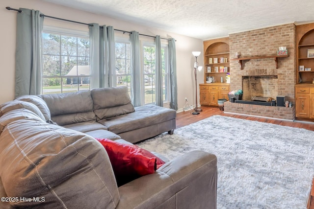 living room featuring a textured ceiling, wood finished floors, baseboards, a brick fireplace, and built in shelves