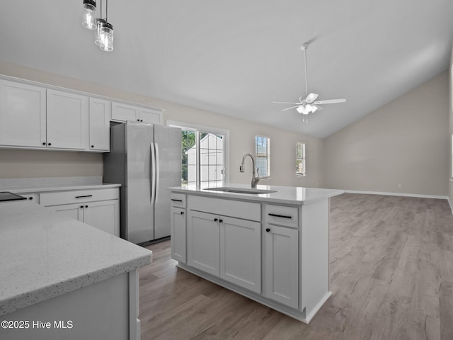 kitchen with a sink, freestanding refrigerator, a ceiling fan, white cabinetry, and vaulted ceiling
