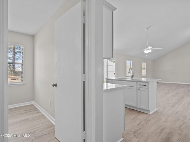 hall featuring baseboards, vaulted ceiling, a sink, and light wood-type flooring