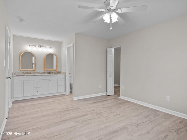 unfurnished bedroom featuring connected bathroom, a sink, light wood-style flooring, and baseboards