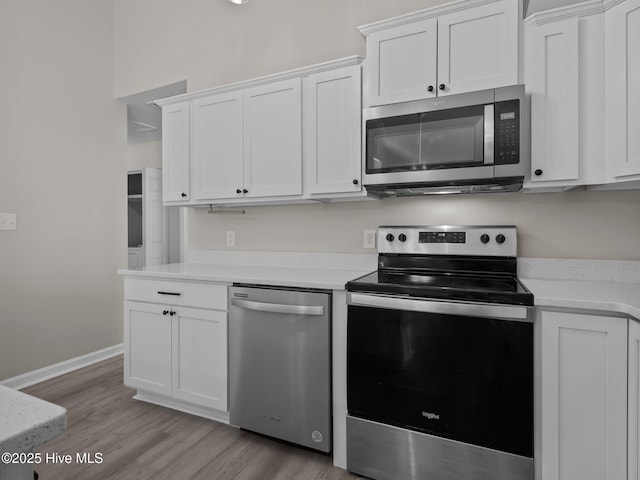 kitchen with baseboards, light wood-type flooring, light countertops, white cabinets, and stainless steel appliances