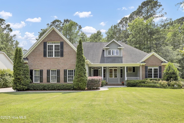 120 E High Bluff Dr, Hampstead, NC 28443 - view of front of house with a front lawn, a porch, brick siding, and roof with shingles