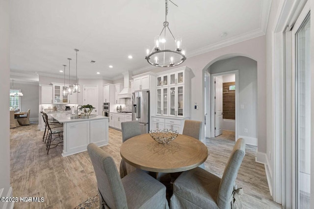 dining room with arched walkways, a notable chandelier, and light wood-type flooring