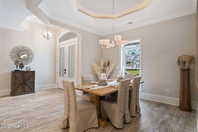 dining space featuring crown molding, a raised ceiling, a chandelier, and wood finished floors