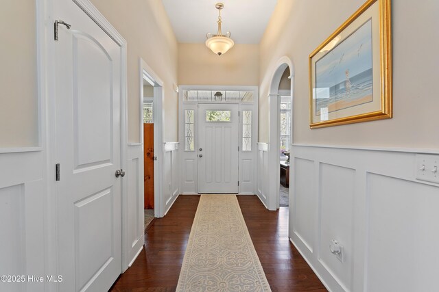 entryway with dark wood-style flooring, a wainscoted wall, and a healthy amount of sunlight
