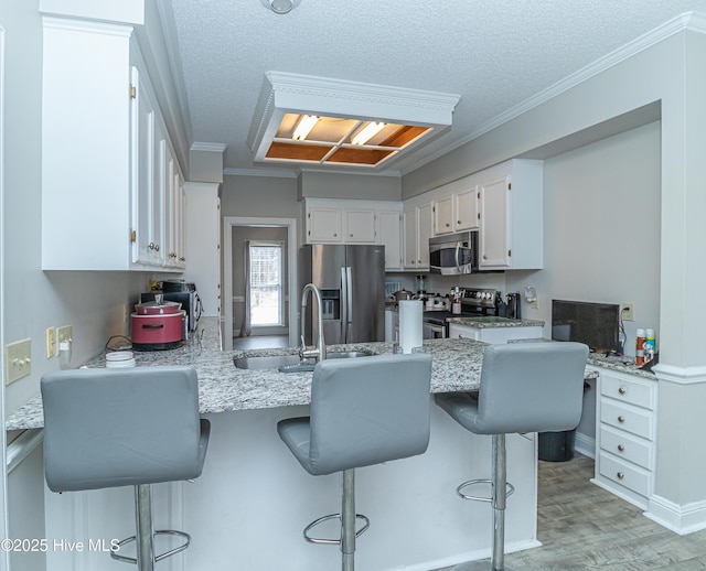 kitchen with light wood-type flooring, ornamental molding, white cabinetry, appliances with stainless steel finishes, and a peninsula