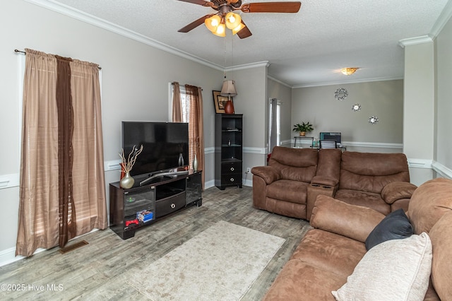 living room with a ceiling fan, wood finished floors, baseboards, a textured ceiling, and crown molding