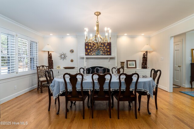 dining area featuring crown molding, an inviting chandelier, light wood finished floors, baseboards, and a brick fireplace