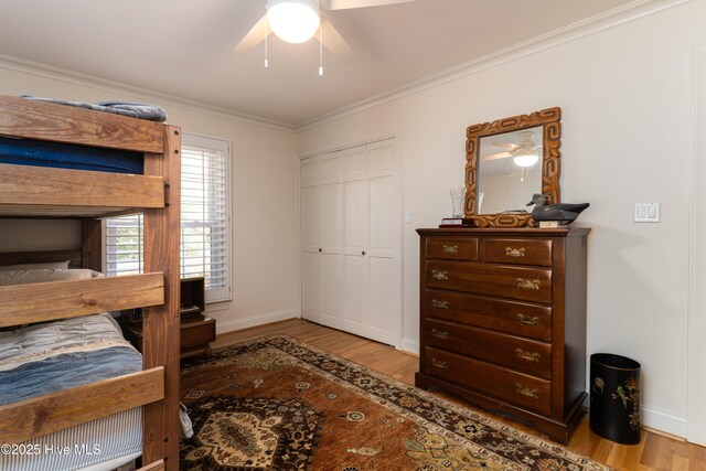 bedroom featuring baseboards, a ceiling fan, wood finished floors, a closet, and crown molding