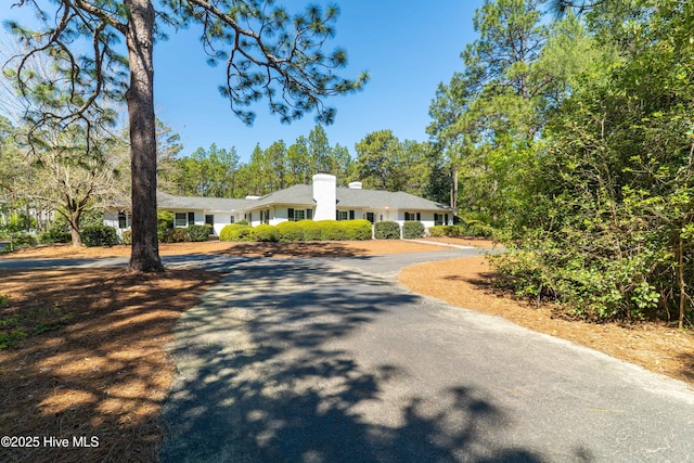 ranch-style home featuring a chimney and curved driveway