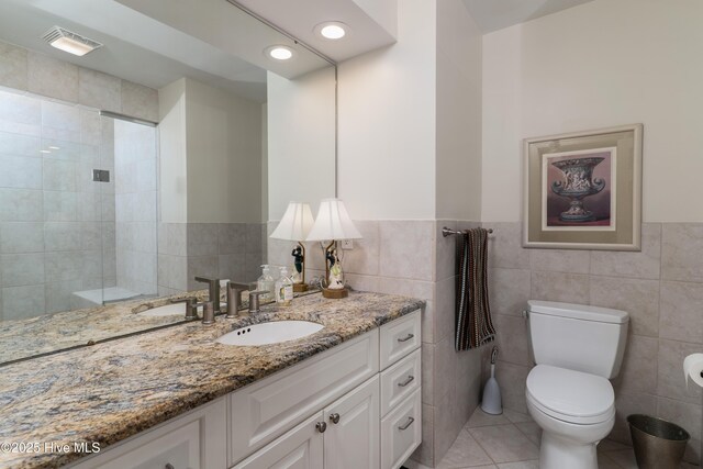 full bath with wainscoting, vanity, tile walls, toilet, and visible vents