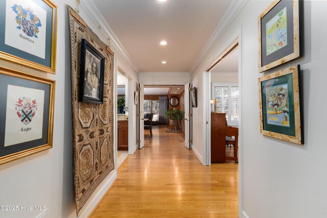 corridor featuring light wood-style floors, a healthy amount of sunlight, baseboards, and ornamental molding