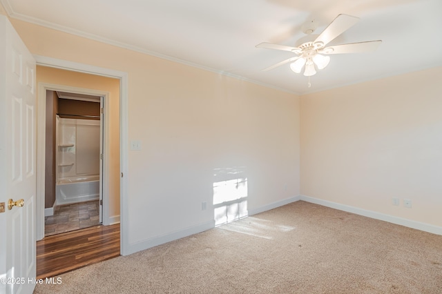 carpeted empty room with baseboards, crown molding, and a ceiling fan