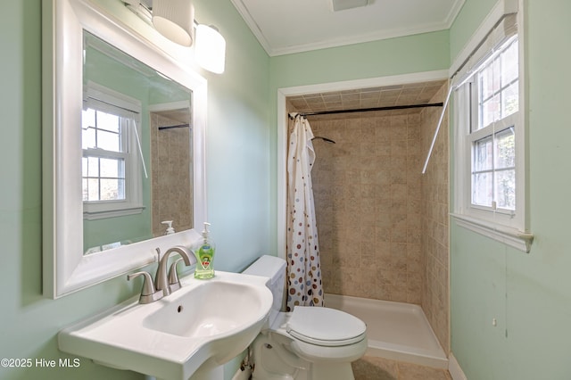bathroom featuring ornamental molding, tiled shower, toilet, and a sink