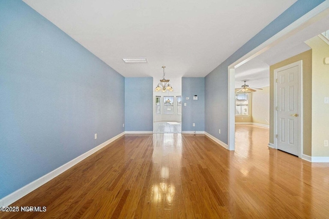 empty room featuring ceiling fan with notable chandelier, visible vents, wood finished floors, and baseboards