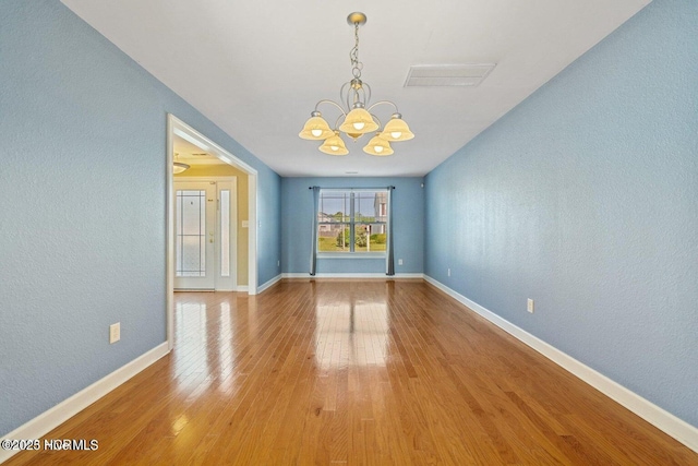 spare room featuring baseboards, visible vents, an inviting chandelier, light wood-style flooring, and a textured wall