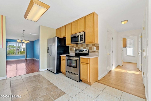 kitchen featuring a chandelier, light countertops, light tile patterned floors, decorative backsplash, and stainless steel appliances