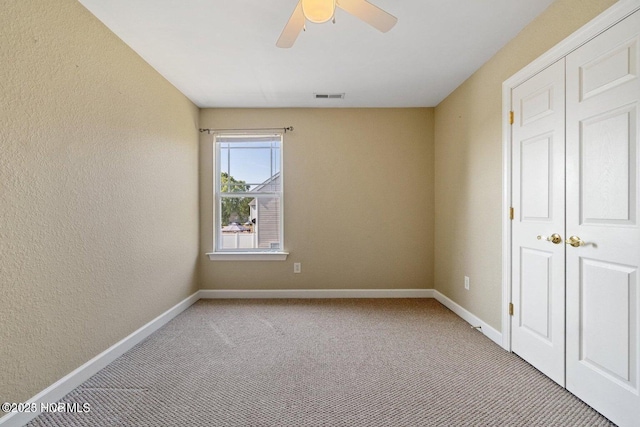 unfurnished bedroom featuring visible vents, baseboards, light carpet, a textured wall, and a ceiling fan