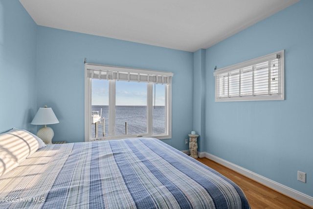 bedroom featuring baseboards, a water view, and wood finished floors