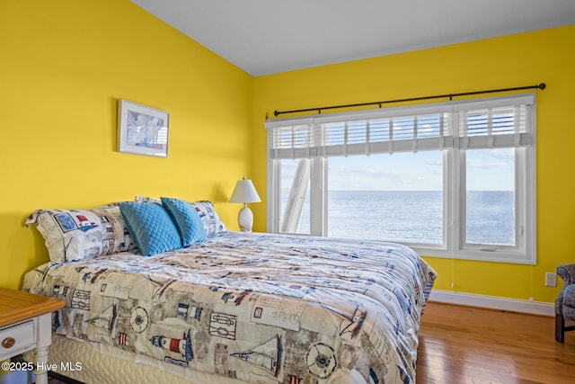 bedroom with a water view, baseboards, and wood finished floors