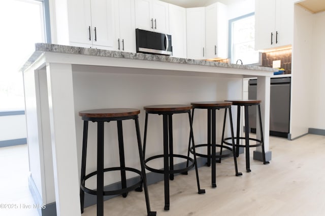 kitchen featuring light wood-style floors, a breakfast bar, stainless steel appliances, light countertops, and white cabinets