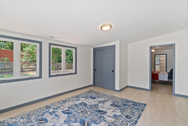 empty room with vaulted ceiling, light wood-style floors, visible vents, and baseboards