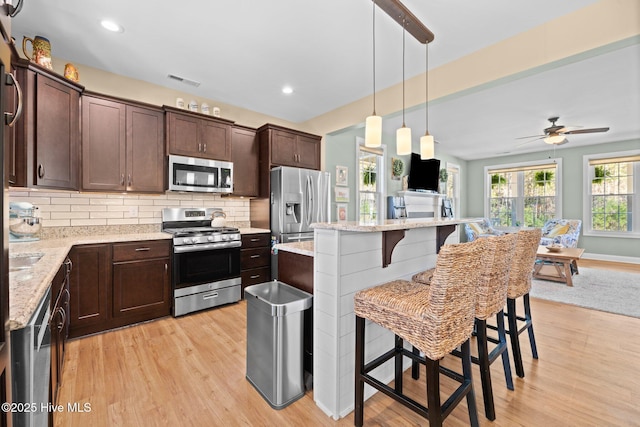 214 Green Trees Dr, New Bern, NC 28560 - kitchen with dark brown cabinetry, a kitchen bar, appliances with stainless steel finishes, tasteful backsplash, and light wood-style flooring
