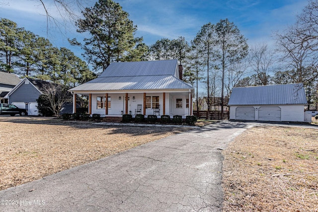 view of front of house with a detached garage, aphalt driveway, covered porch, metal roof, and an outbuilding