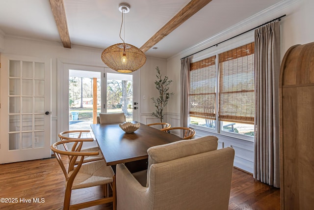 dining room featuring wood finished floors, beam ceiling, wainscoting, crown molding, and a decorative wall