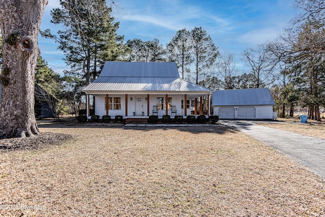 view of front facade with a detached garage, aphalt driveway, a porch, metal roof, and an outdoor structure