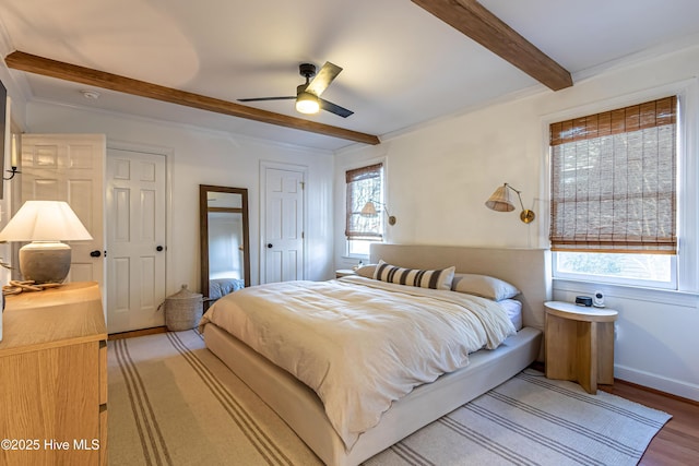bedroom featuring light wood finished floors, beamed ceiling, multiple windows, and baseboards