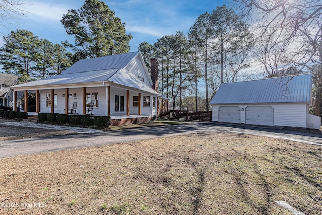 view of property exterior featuring covered porch, a chimney, an outdoor structure, aphalt driveway, and metal roof