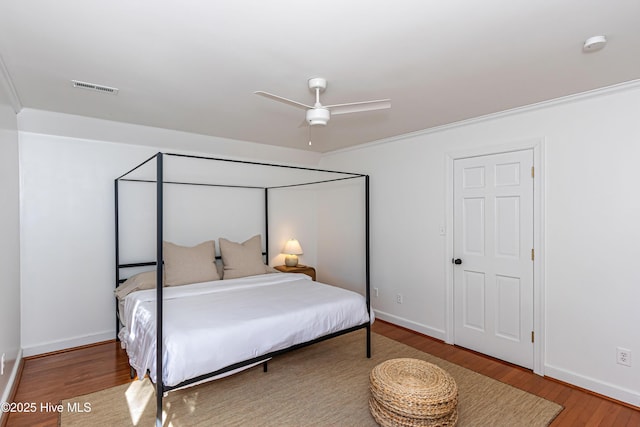 bedroom with visible vents, baseboards, wood finished floors, and ornamental molding