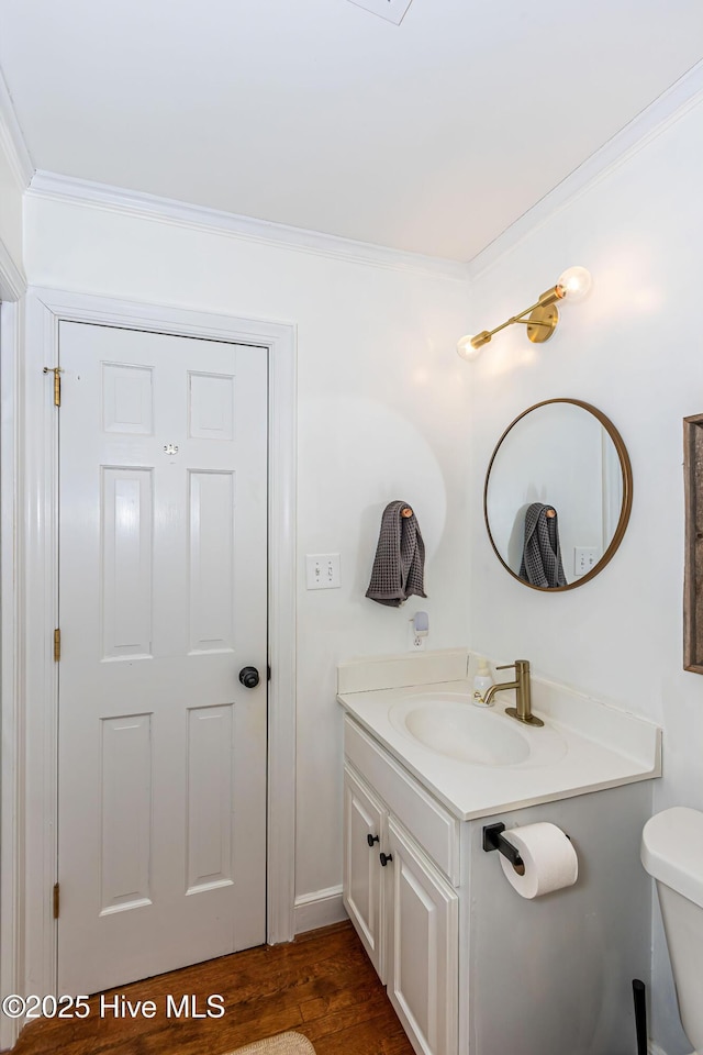 half bath with wood finished floors, toilet, vanity, and ornamental molding