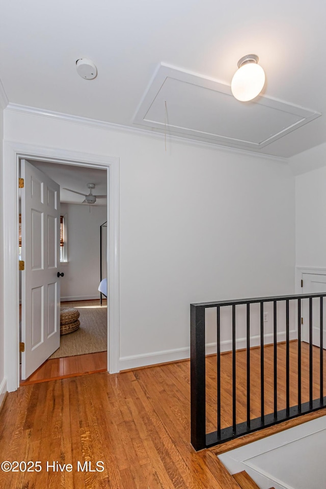 hallway featuring attic access, wood finished floors, baseboards, and ornamental molding