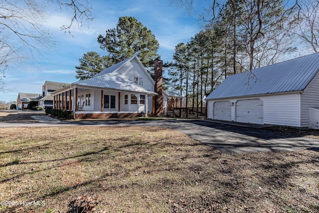 exterior space featuring an outbuilding, a detached garage, fence, metal roof, and a chimney