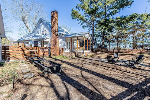 back of property featuring ceiling fan, a chimney, a fenced backyard, and a garden