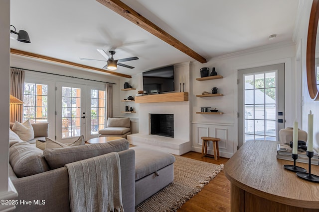 living room featuring beam ceiling, a ceiling fan, wood finished floors, a large fireplace, and crown molding