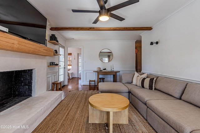living room featuring wood finished floors, beam ceiling, ornamental molding, and a ceiling fan