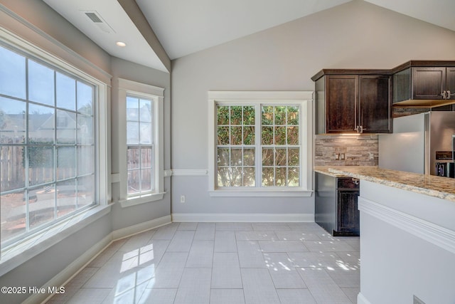 kitchen with tasteful backsplash, dark brown cabinets, light stone counters, stainless steel fridge with ice dispenser, and lofted ceiling