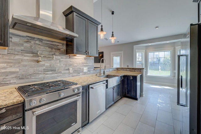 kitchen with a sink, wall chimney exhaust hood, a peninsula, tasteful backsplash, and appliances with stainless steel finishes