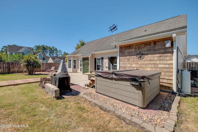 back of property with roof with shingles, a fenced backyard, a hot tub, a yard, and a patio