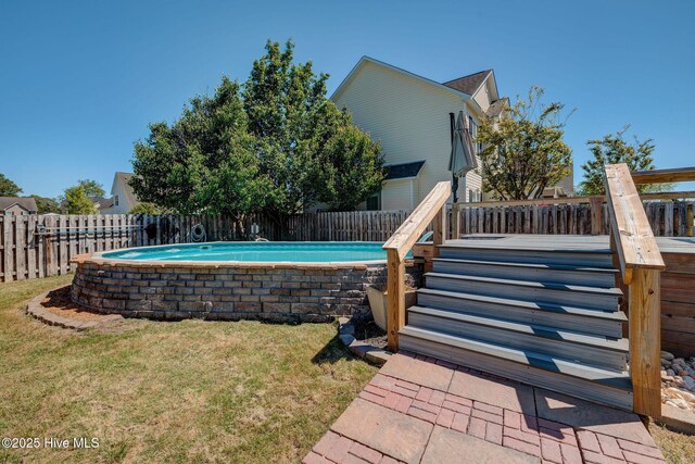 view of swimming pool featuring a lawn, a wooden deck, a fenced backyard, and a fenced in pool