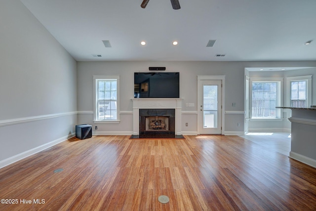 unfurnished living room featuring baseboards, a ceiling fan, wood finished floors, and a fireplace