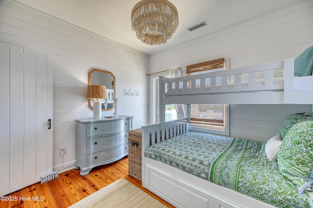 bedroom with visible vents, wood walls, and wood finished floors