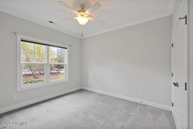 carpeted empty room with crown molding, baseboards, a ceiling fan, and visible vents