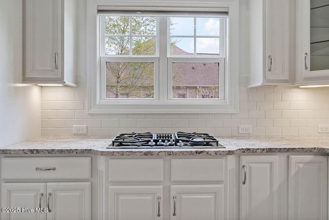 kitchen with tasteful backsplash, light stone counters, gas stovetop, glass insert cabinets, and white cabinets