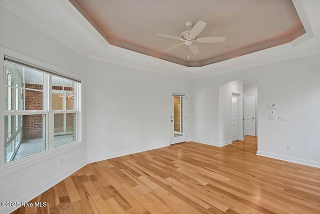 spare room featuring ceiling fan, arched walkways, a raised ceiling, light wood finished floors, and baseboards