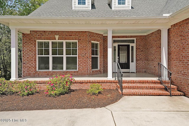 property entrance featuring brick siding, covered porch, and roof with shingles