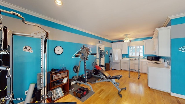 exercise room with light wood-type flooring, crown molding, and a ceiling fan
